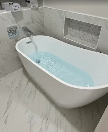 Freestanding soaking tub with wall-mounted filler and marble tile surround